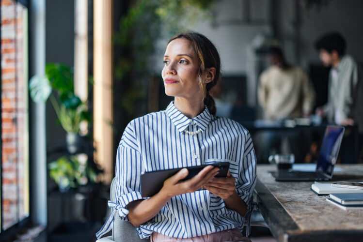 Photographie d'une femme, tablette à la main, qui regarde vers l'horizon.